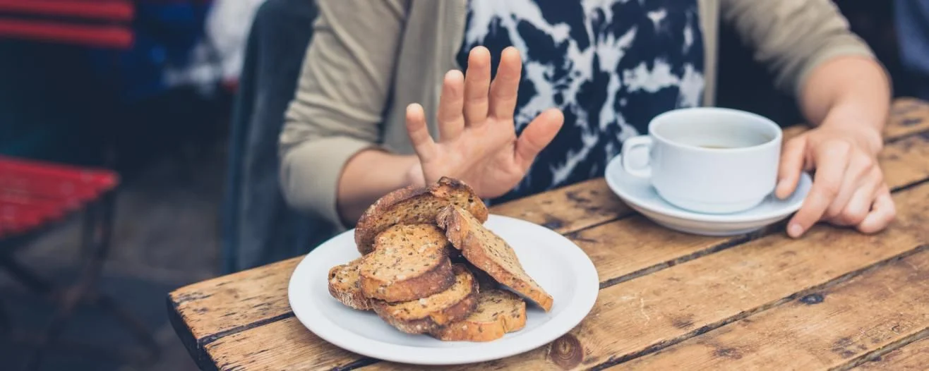 A hand gestures "no" beside a plate stacked with cookies and a cup of coffee on a rustic wooden table