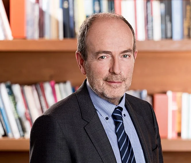 Man in a suit and tie poses confidently in front of a bookshelf filled with various books
