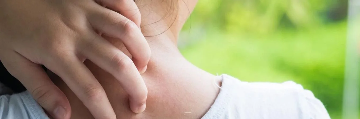 A hand gently scratches the back of a neck, with a blurred green background indicating an outdoor setting