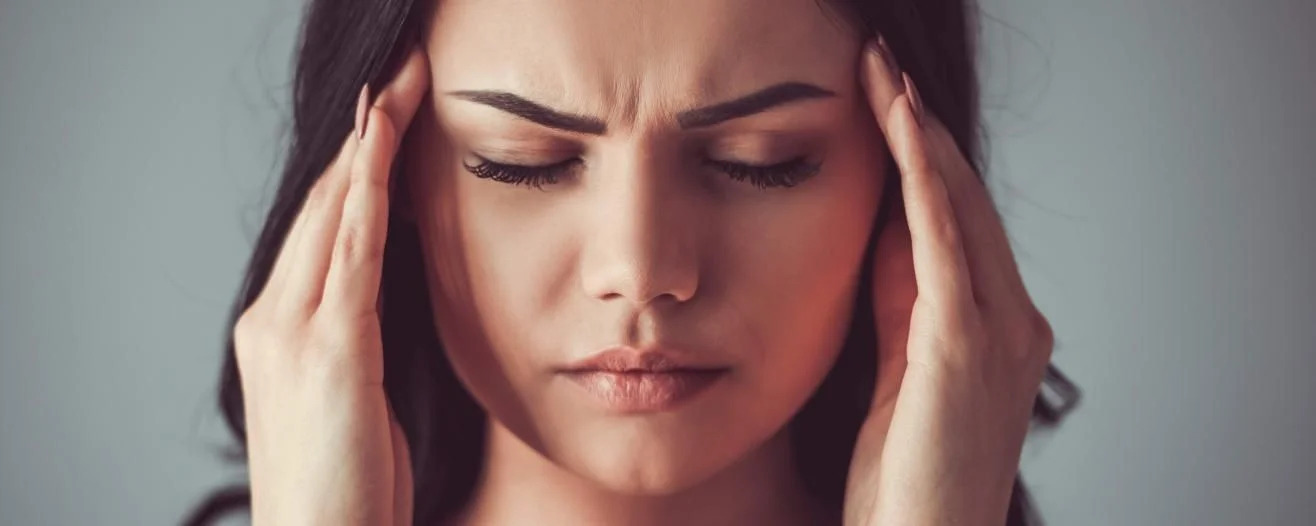 Woman with long dark hair frowns, pressing her temples with her fingertips, conveying a sense of discomfort or headache