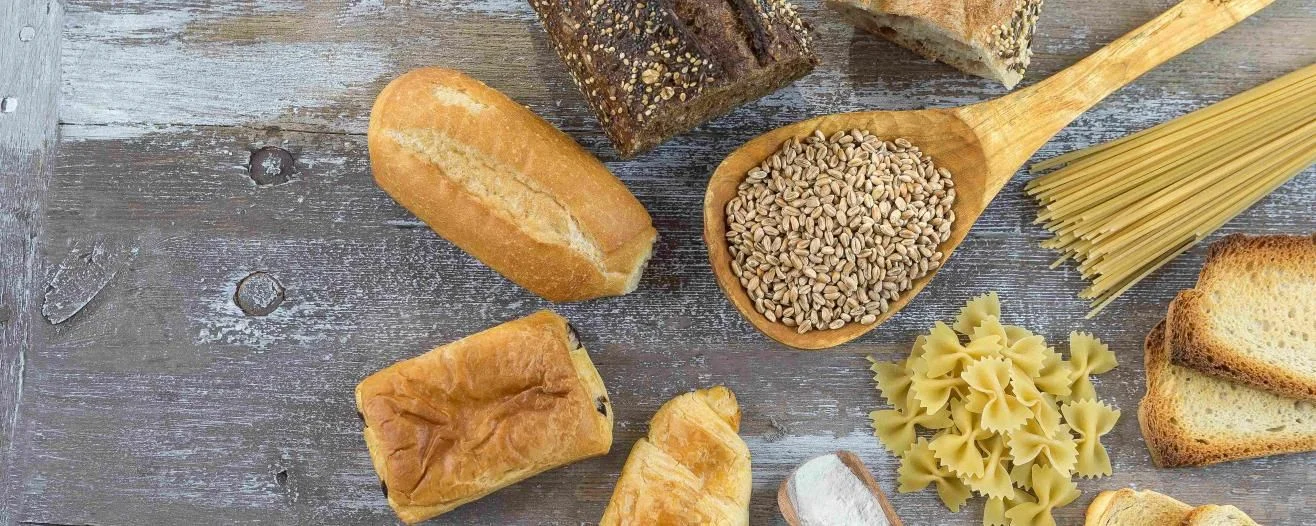 An assortment of breads, grains, and pasta arranged on a rustic wooden surface, highlighting diverse textures and shapes
