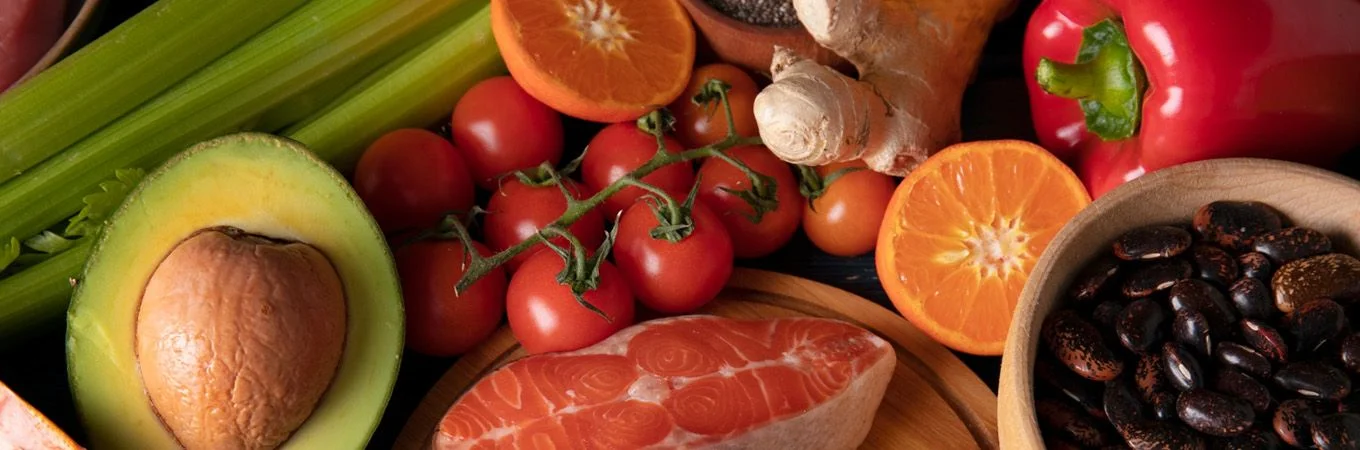 Colorful assortment of fresh ingredients including avocado, tomatoes, oranges, ginger, celery, bell pepper, and beans