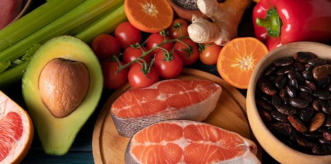 Fresh salmon fillets on a wooden plate surrounded by vibrant fruits and vegetables, including avocado, tomatoes, and beans